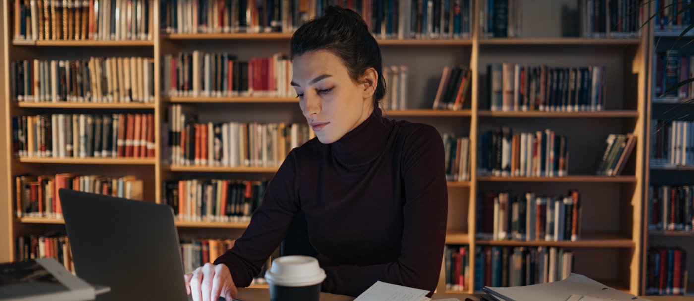 Una mujer con un portátil y estanterías con libros detrás
